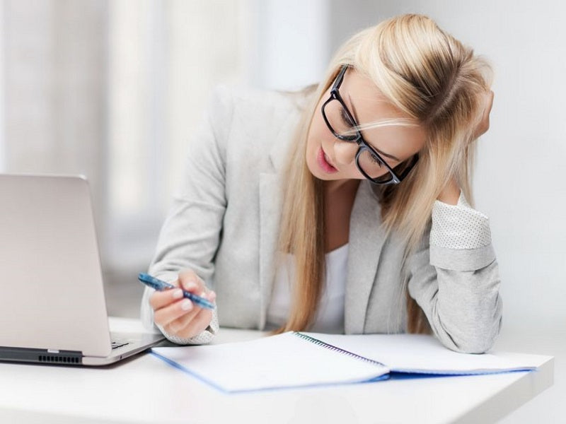 Woman writing at a desk beside a laptop