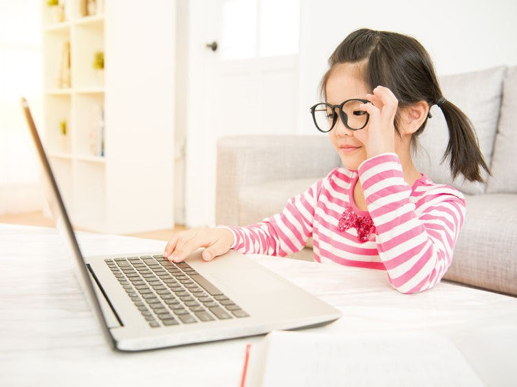 Child wearing glasses using a laptop