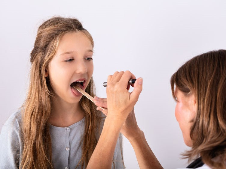 Clinician examining a child's mouth with a tongue depressor